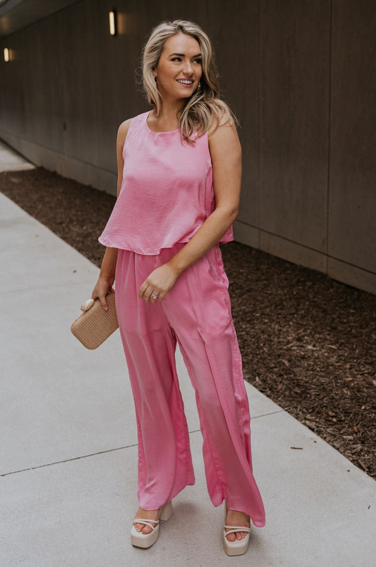 Full body view of female model wearing the Rowan Pink Sleeveless Jumpsuit which features Pink Satin Fabric, Wide Pant Legs, Round Neckline, Sleeveless and Back Key Hole with Button Closure