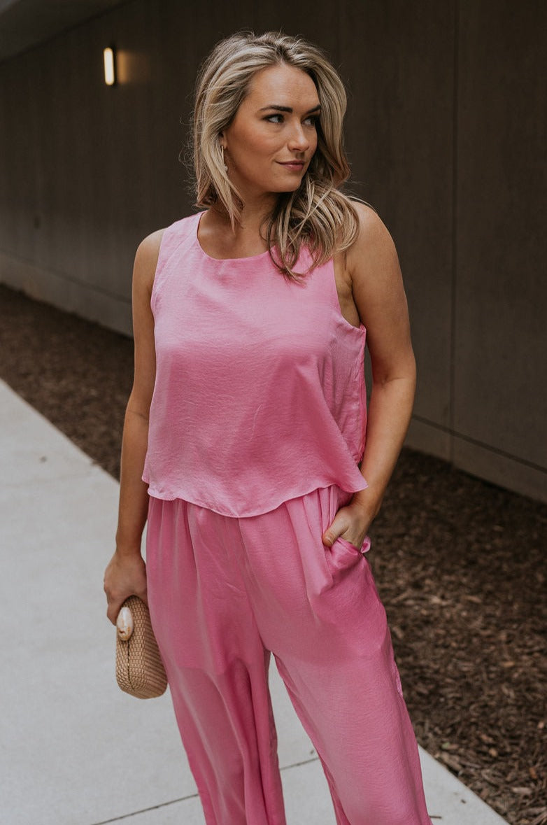 Front view of female model wearing the Rowan Pink Sleeveless Jumpsuit which features Pink Satin Fabric, Wide Pant Legs, Round Neckline, Sleeveless and Back Key Hole with Button Closure