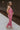 Full body side view of female model wearing the Rowan Pink Sleeveless Jumpsuit which features Pink Satin Fabric, Wide Pant Legs, Round Neckline, Sleeveless and Back Key Hole with Button Closure