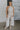 Full body view of female model wearing the Lilah Natural Linen Halter Neckline Jumpsuit which features Natural Linen Fabric, Wide Pant Legs, Tie Waistband, Twist Halter Neckline with Button Closure and Back Key Hole Design