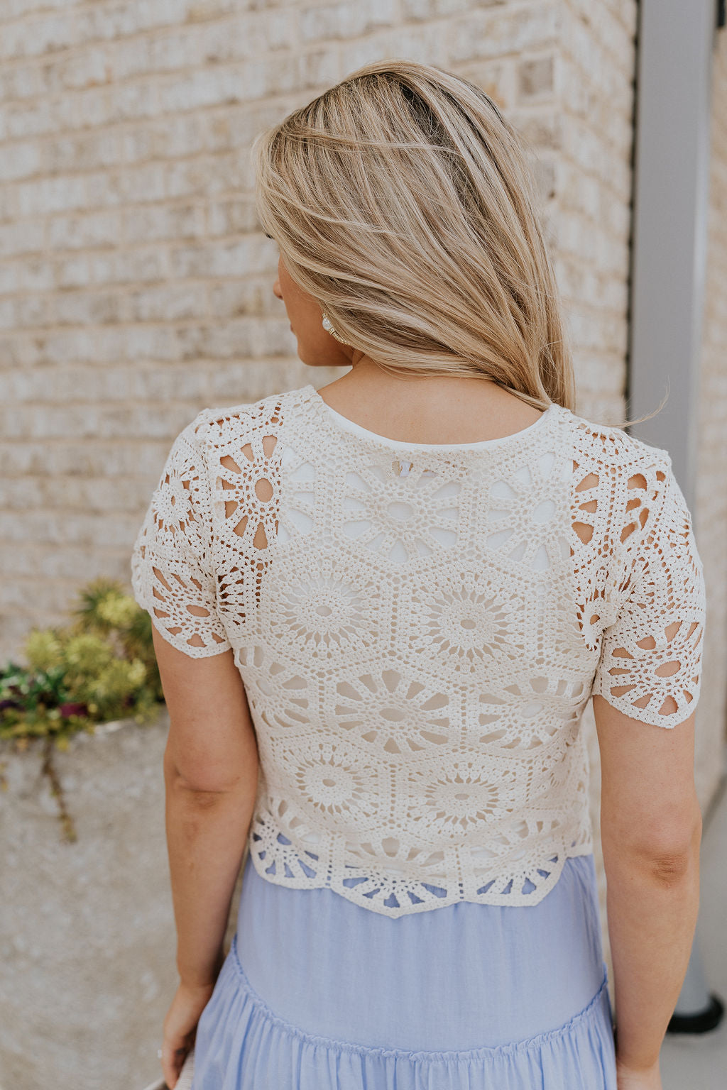 Back view of female model wearing the Brynlee Cream Crochet Scallop Top which features Cream Crochet Fabric, Cropped Waist, Round Neckline and Short Sleeves