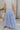 Back view of female model wearing the Alana Periwinkle Tiered Maxi Skirt which features Periwinkle Lightweight Fabric, Maxi Length, Periwinkle Thigh Length Lining, Tiered Body and Elastic Waistband with Drawstring Ties