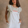 Front view of female model wearing the Kassidy White Denim Sleeveless Romper which features White Cotton Fabric, Two Front Pockets, Two Back Pockets, Fray Hem, Adjustable Tie Straps and Sleeveless