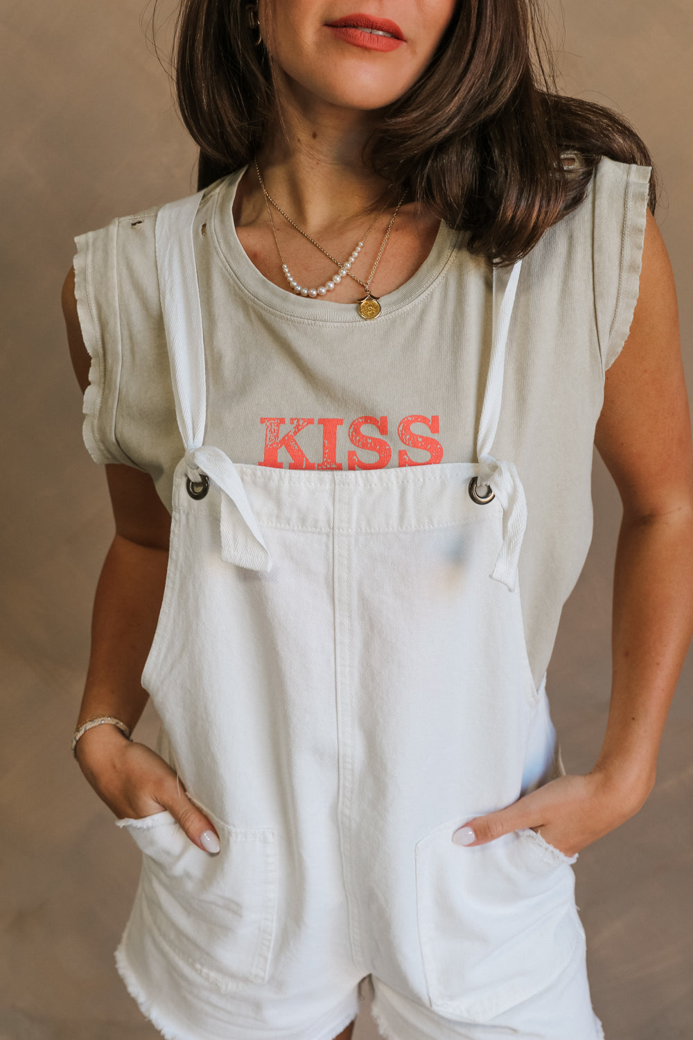 Close up view of female model wearing the Kassidy White Denim Sleeveless Romper which features White Cotton Fabric, Two Front Pockets, Two Back Pockets, Fray Hem, Adjustable Tie Straps and Sleeveless