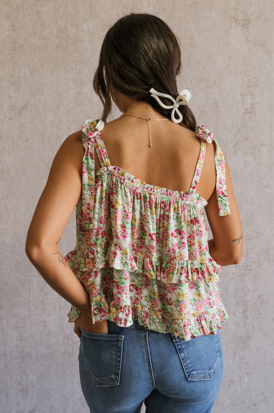 Back view of female model wearing the Florence Pink Multi Floral Tie Strap Tank which features features Pink, Yellow, Green and White Floral Print, Ruffle Tiered Details, Square Neckline and Tie Straps