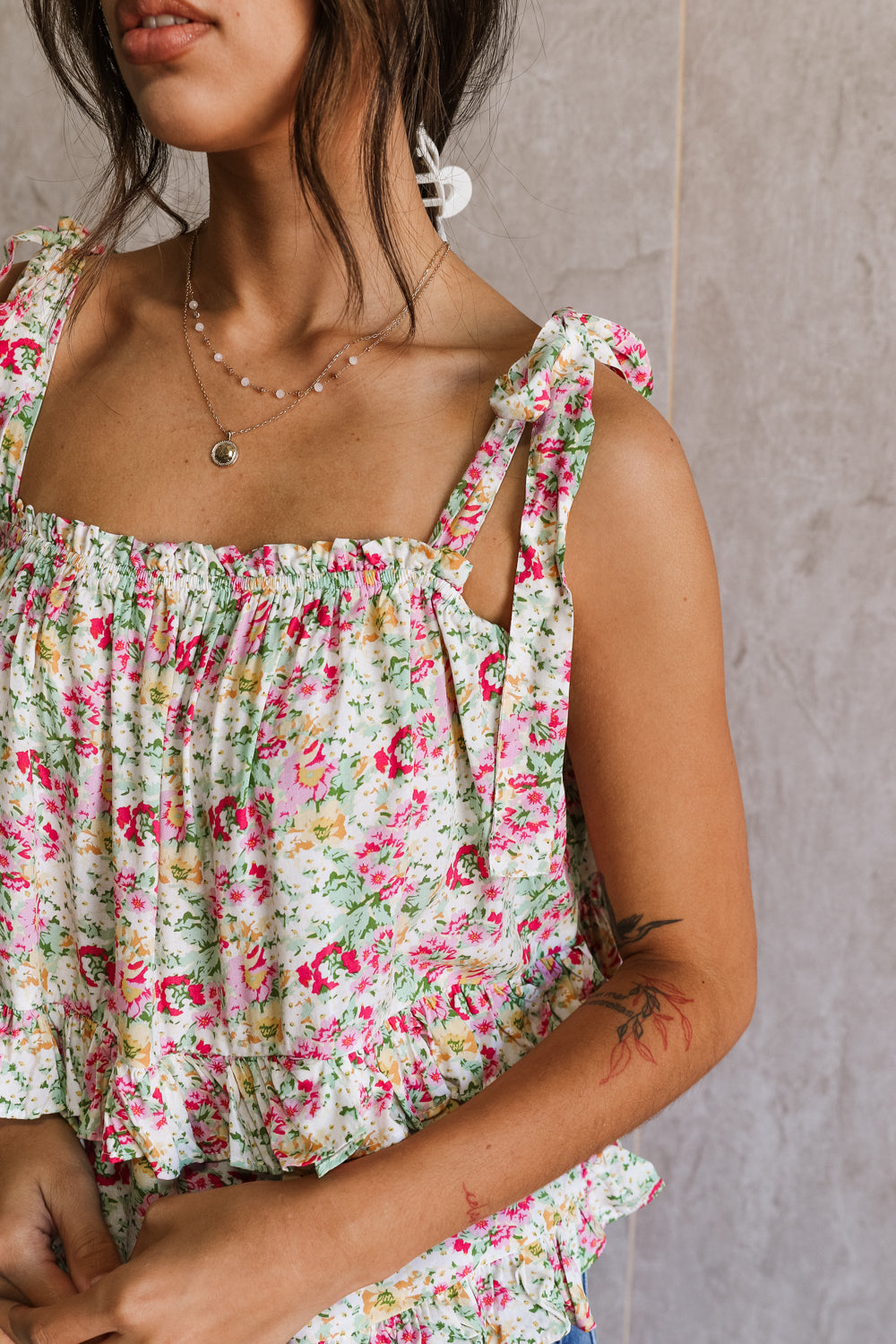 Close up view of female model wearing the Florence Pink Multi Floral Tie Strap Tank which features features Pink, Yellow, Green and White Floral Print, Ruffle Tiered Details, Square Neckline and Tie Straps