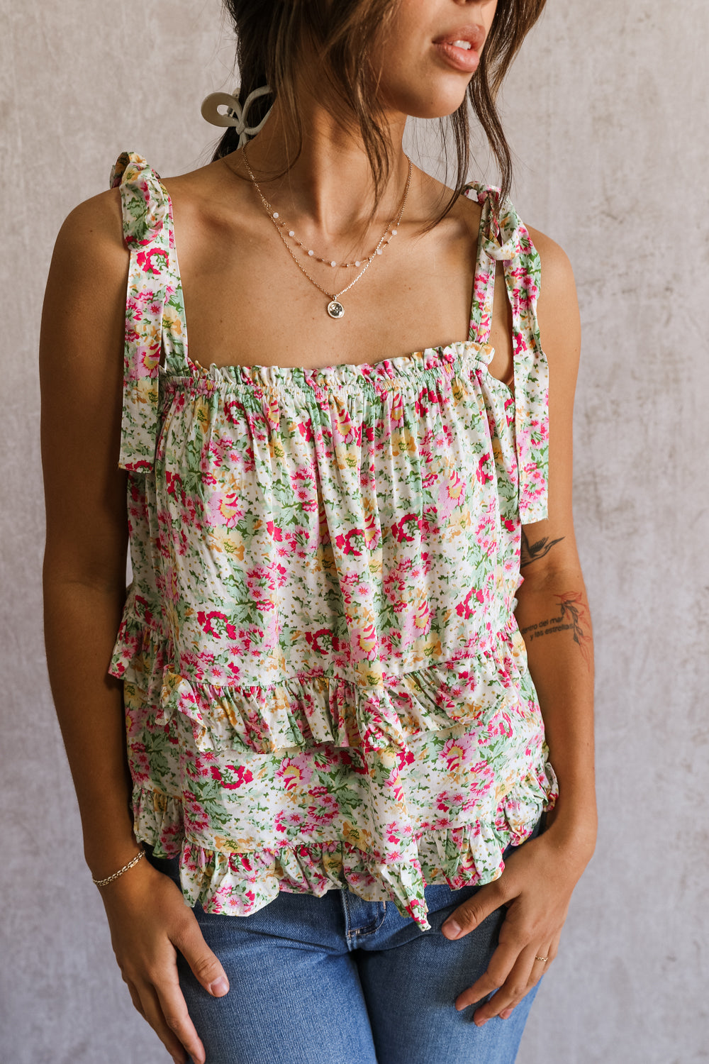 CLose up view of female model wearing the Florence Pink Multi Floral Tie Strap Tank which features features Pink, Yellow, Green and White Floral Print, Ruffle Tiered Details, Square Neckline and Tie Straps