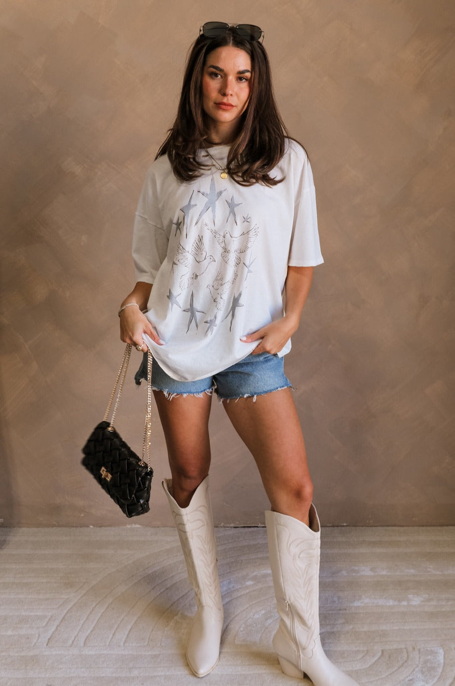 Full body view of female model wearing the Stars and Birds White Distressed Graphic Top which features  White Cotton Fabric, Distressed Details, Short Sleeves, Round Neckline and Stars and Birds Graphic