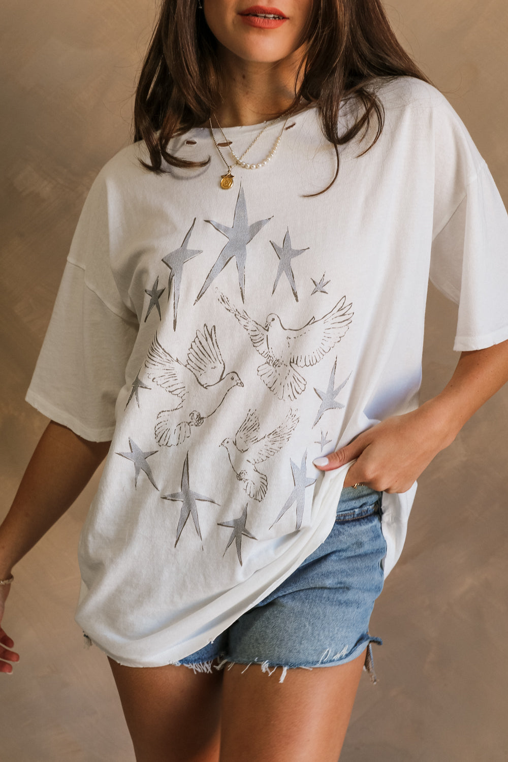 Close up view of female model wearing the Stars and Birds White Distressed Graphic Top which features White Cotton Fabric, Distressed Details, Short Sleeves, Round Neckline and Stars and Birds Graphic