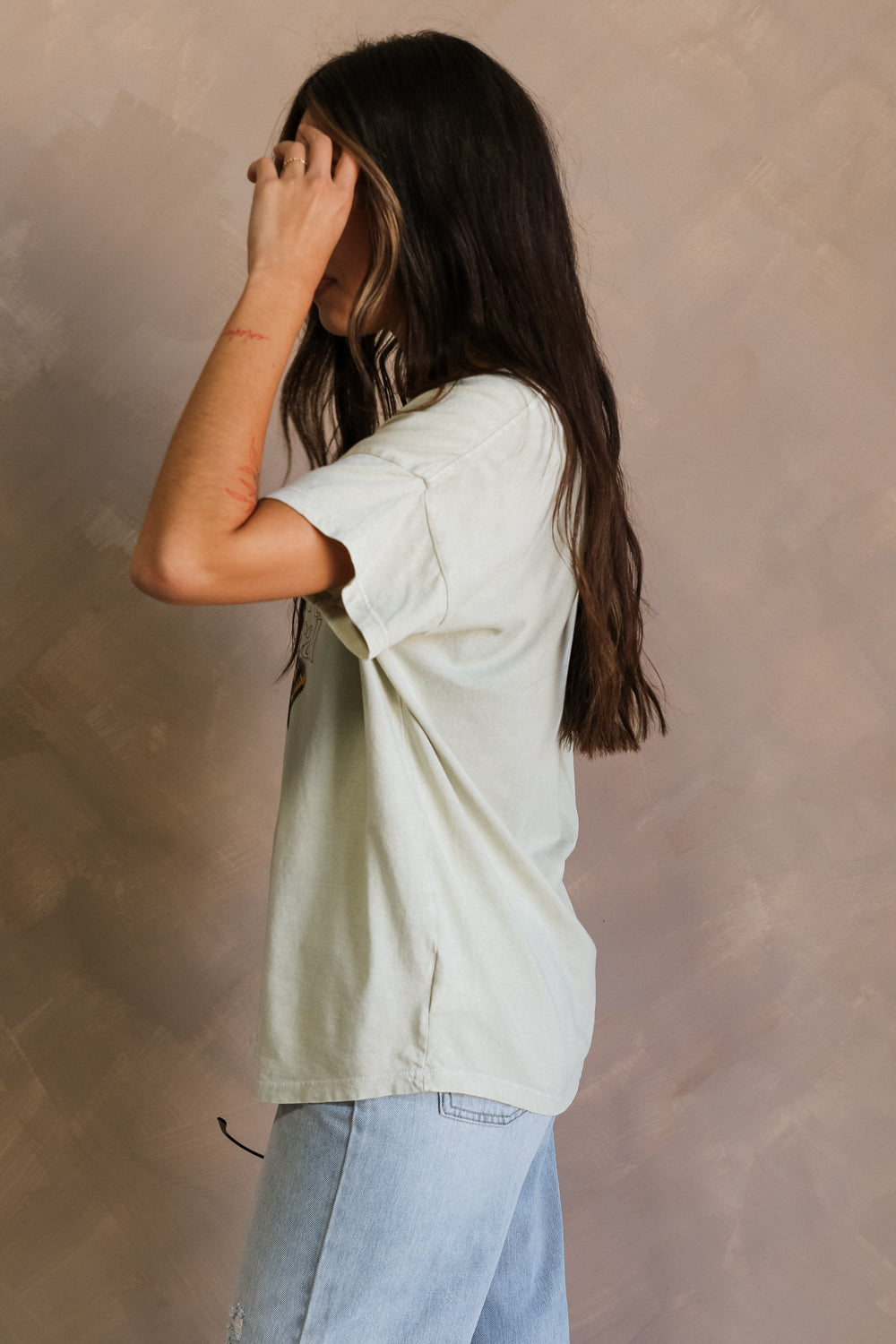 Side view of female model wearing the Los Angeles Musical Light Sage Graphic Top which features Light Sage Cotton Fabric, Short Sleeve Top, Round Neckline and Los Angeles, CA Musical Graphic