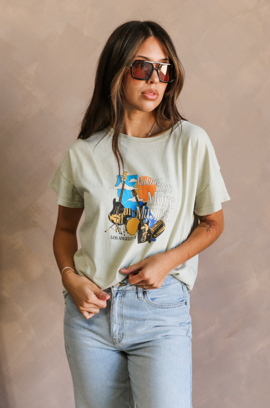 Front view of female model wearing the Los Angeles Musical Light Sage Graphic Top which features Light Sage Cotton Fabric, Short Sleeve Top, Round Neckline and Los Angeles, CA Musical Graphic