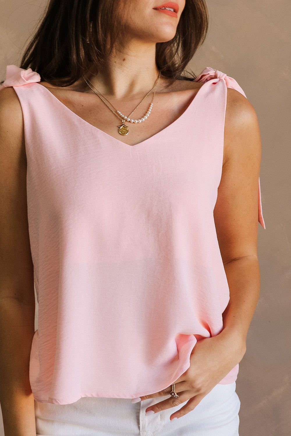 Close front view of female model wearing the Jenna Blush Tie Strap Tank Top that has lightweight blush fabric, tie straps, and a v neck. 