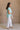 Full body side view of female model wearing the Amalia Collared Short Sleeve Top in mint, which has short sleeves and a collar neckline. Paired with white capris. Model is holding white purse.