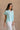 Frontal side view of female model wearing the Amalia Collared Short Sleeve Top in mint, which has short sleeves and a collar neckline. Paired with white capris. Model is holding white purse.
