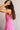 Side view of female model wearing the Valery Pink Cropped Tank which features Pink Cotton Fabric, Cropped Waist, Upper Pleated Details, V-Neckline, Sleeveless and Back Tie Closure with Light Wood Beads