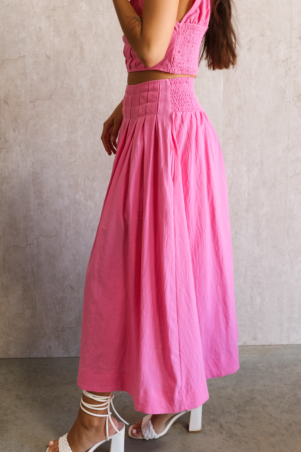 Side view of female model wearing the Valery Pink Tiered Midi Skirt which features Pink Cotton Fabric, Pink Lining, Upper Pleated Details and Smocked Waistband