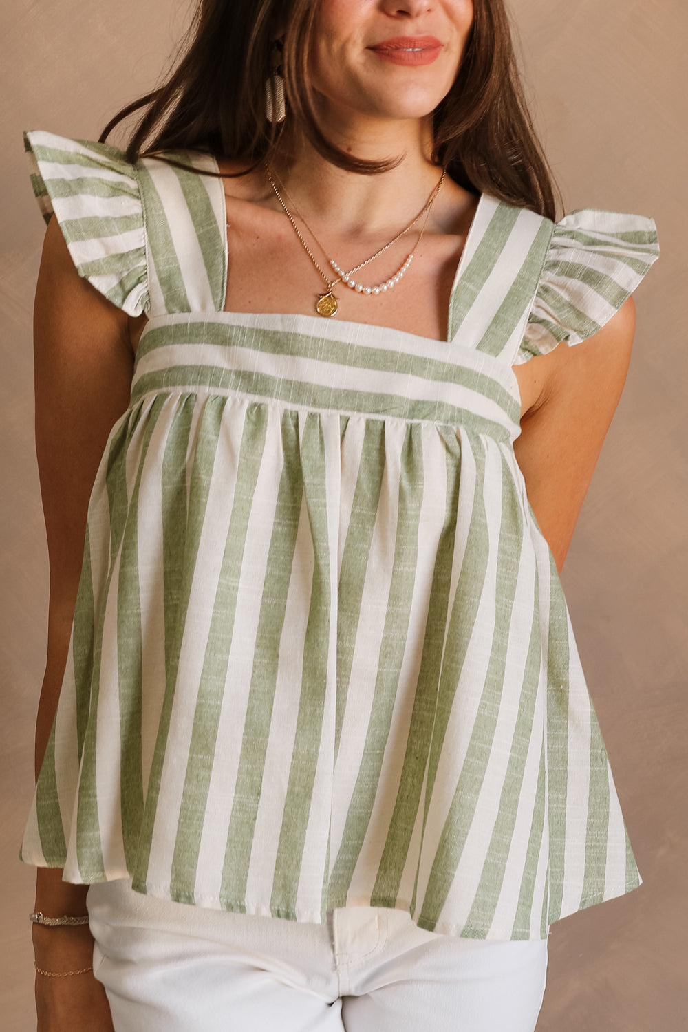 Close front view of female model wearing the Coraline that has green and ivory stripes, ruffled straps, and a cropped babydoll fit. 