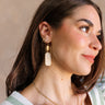 Side of female model's face; model is wearing the Addison Gold & Pearl Dangle Earrings that have a gold hexagon shape attached to gold hooks, with a gold hexagonal dangle with pearls on top.