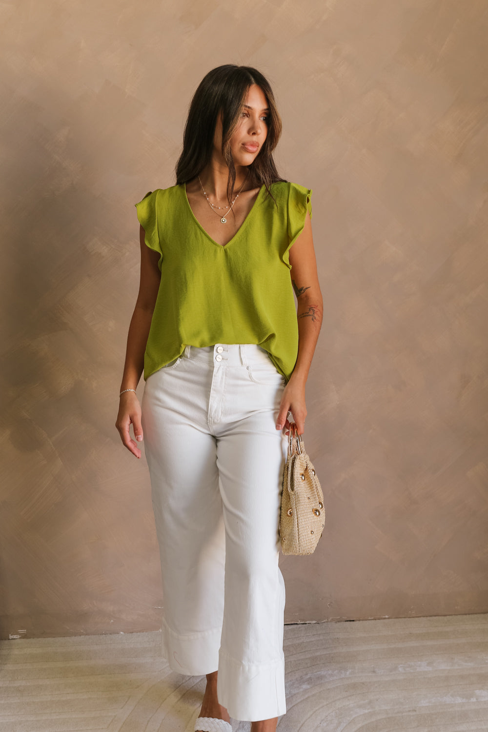 Full body front view of female model wearing the Marceline Chartreuse Ruffled Top that has bright chartreuse green fabric, ruffled sleeve trim, and a v neck. Top is front tucked