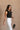 Side view of model wearing the Oakley White Sleeveless Top which features black fabric, cropped waist, scooped neckline, thick straps and sleeveless.