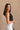 Side view of model wearing the Oakley White Sleeveless Top which features black fabric, cropped waist, scooped neckline, thick straps and sleeveless.