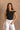 Close-up front view of model wearing the Oakley White Sleeveless Top which features black fabric, cropped waist, scooped neckline, thick straps and sleeveless.