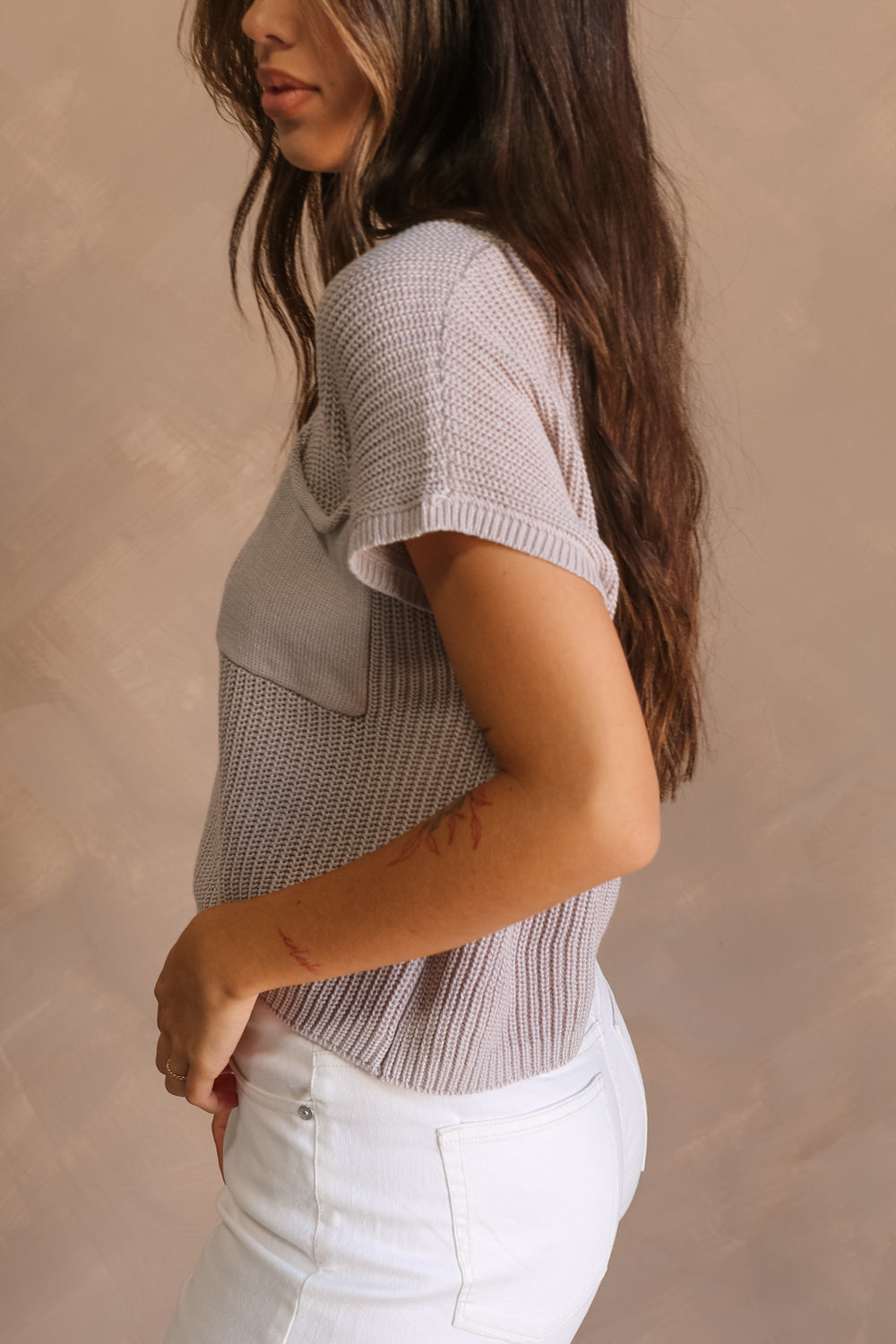 Side view of female model wearing the Harper Grey Knit Short Sleeve Top which features Grey Small Cable Knit Fabric, Left Front Chest Pocket, Round Neckline and Short Sleeves