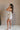 Side view of female model wearing the Elodie Beige Ruffle Tier Sleeveless Romper which features Beige Lightweight Fabric, Beige Lining, Ruffle Tier Details, Round Neckline, Sleeveless and Back Button Closure