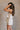 Side view of female model wearing the Elodie Beige Ruffle Tier Sleeveless Romper which features Beige Lightweight Fabric, Beige Lining, Ruffle Tier Details, Round Neckline, Sleeveless and Back Button Closure