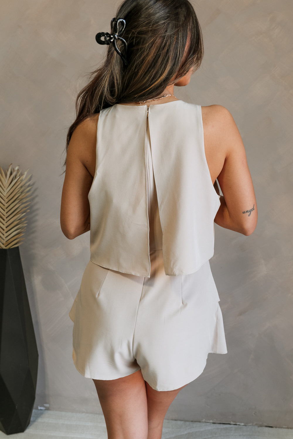 Back view of female model wearing the Elodie Beige Ruffle Tier Sleeveless Romper which features Beige Lightweight Fabric, Beige Lining, Ruffle Tier Details, Round Neckline, Sleeveless and Back Button Closure