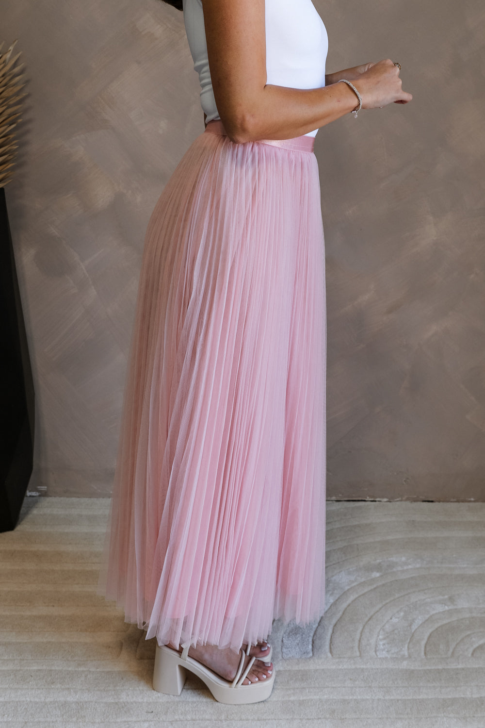 Side view of female model wearing the Adele Dusty Pink Pleated Tulle Midi Skirt which features Dusty Pink Tulle Pleated Fabric, Dusty Pink Lining, Midi Length and Satin Elastic Band