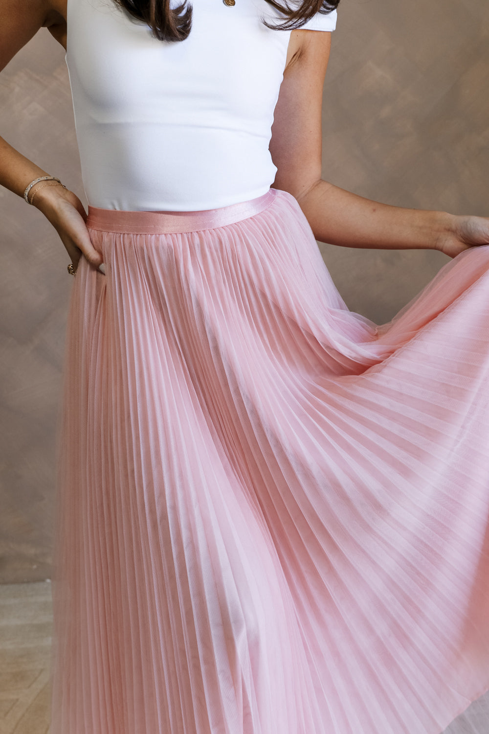 Close up view of female model wearing the Adele Dusty Pink Pleated Tulle Midi Skirt which features Dusty Pink Tulle Pleated Fabric, Dusty Pink Lining, Midi Length and Satin Elastic Band