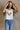 Front view of female model wearing the Free Bird Smoke Cropped Tank which features Cream Cotton Fabric, Cropped Lettuce Hem, Round Neckline, Sleeveless and Eagle Graphic