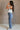 Full body side view of female model wearing the Free Bird Smoke Cropped Tank which features Cream Cotton Fabric, Cropped Lettuce Hem, Round Neckline, Sleeveless and Eagle Graphic