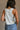 Back view of female model wearing the Free Bird Smoke Cropped Tank which features Cream Cotton Fabric, Cropped Lettuce Hem, Round Neckline, Sleeveless and Eagle Graphic