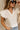 Front view of female model wearing the Jemma White Ruffle Top that has white fabric, short ruffled cap sleeves, a v neckline, and keyhole back. 