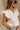 Side view of female model wearing the Jemma White Ruffle Top that has white fabric, short ruffled cap sleeves, a v neckline, and keyhole back. Worn with blue jeans.