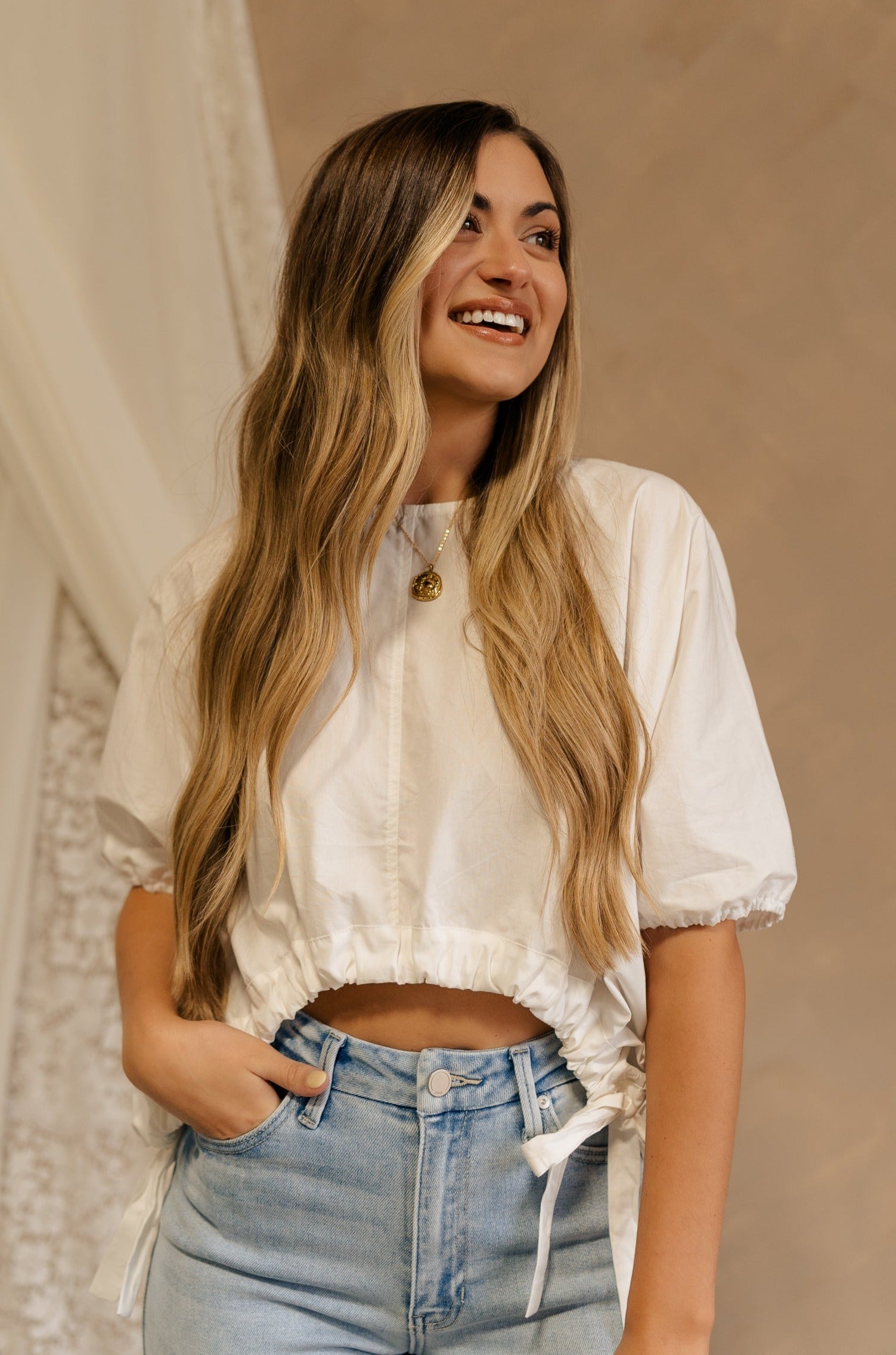 Front view of female model wearing the Karina Drawstring Cropped Short Sleeve Top in white. This top has white fabric, short sleeves with elastic trim, and a cropped drawstring waist with ties.