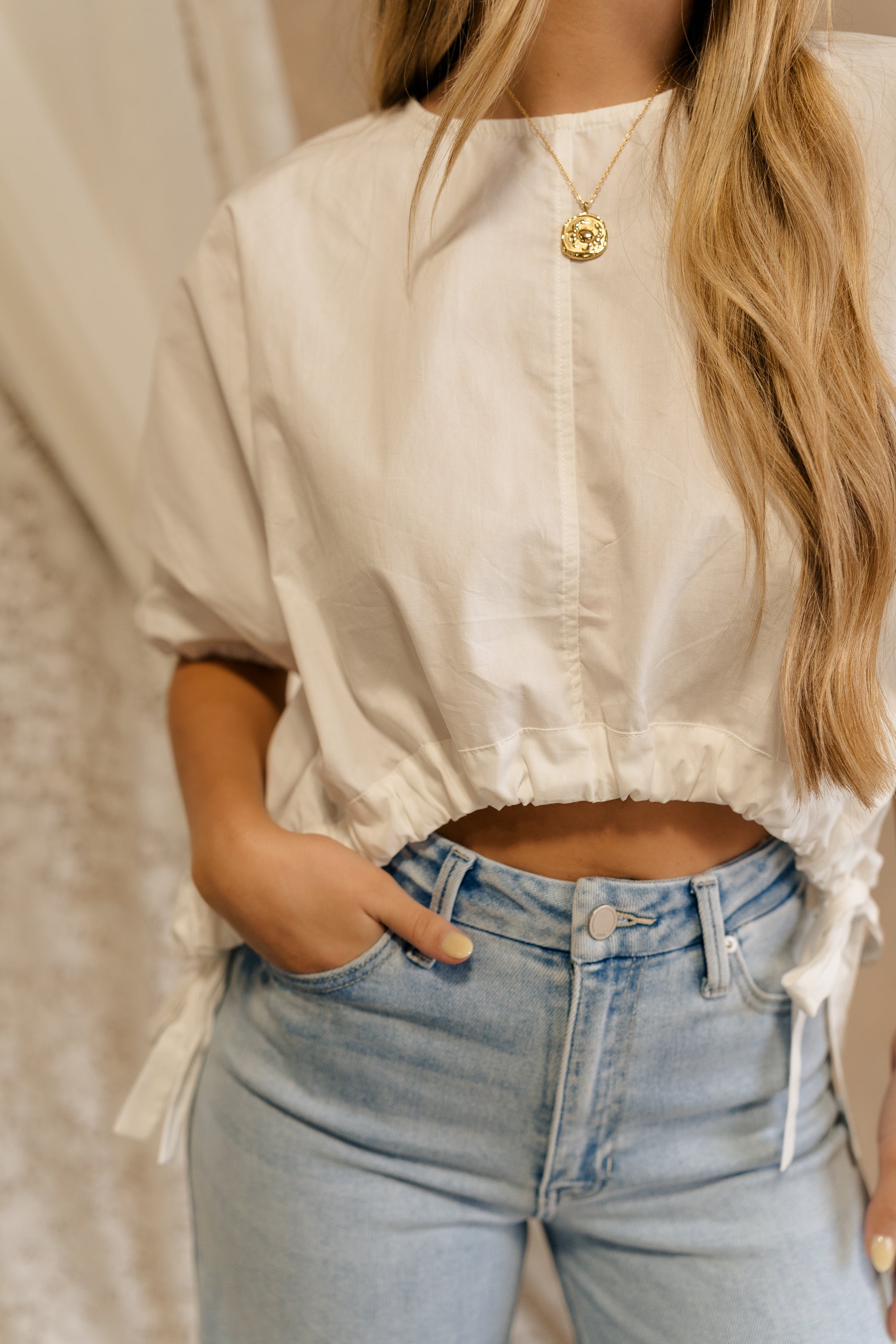 Close-up front view of female model wearing the Karina Drawstring Cropped Short Sleeve Top in white. This top has white fabric, short sleeves with elastic trim, and a cropped drawstring waist with ties.