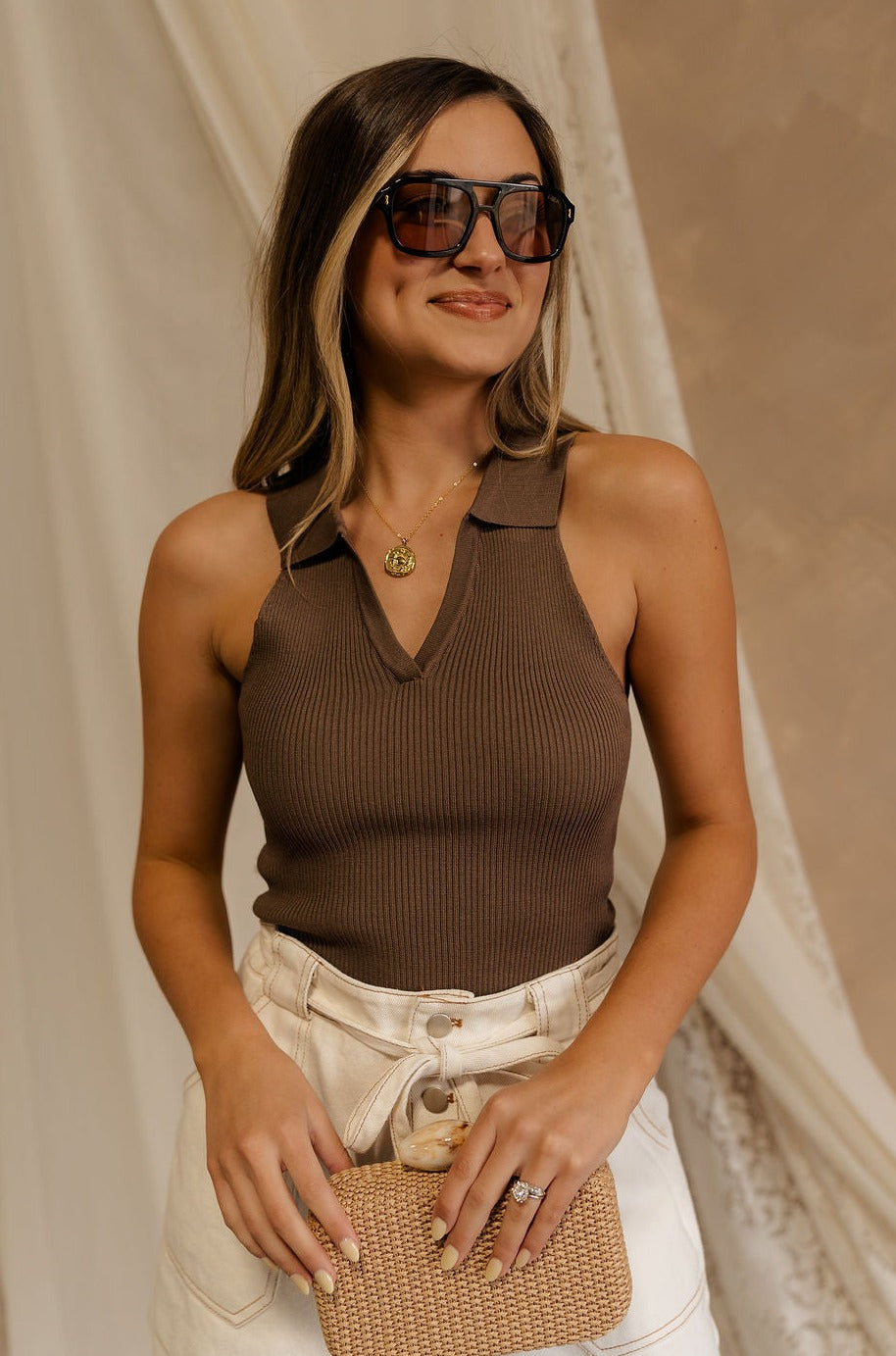 Front view of female model wearing the Maisie Ribbed Collar Tank in brown that feature brown ribbed fabric and a collared sleeveless neckline. Paired with white shotrs