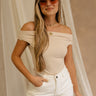 Front view of female model wearing the Isabella Off The Shoulder Cropped Tank in beige, that features off the shoulder short sleeves, a straight neckline, and a cropped waist. Paired with white jeans.