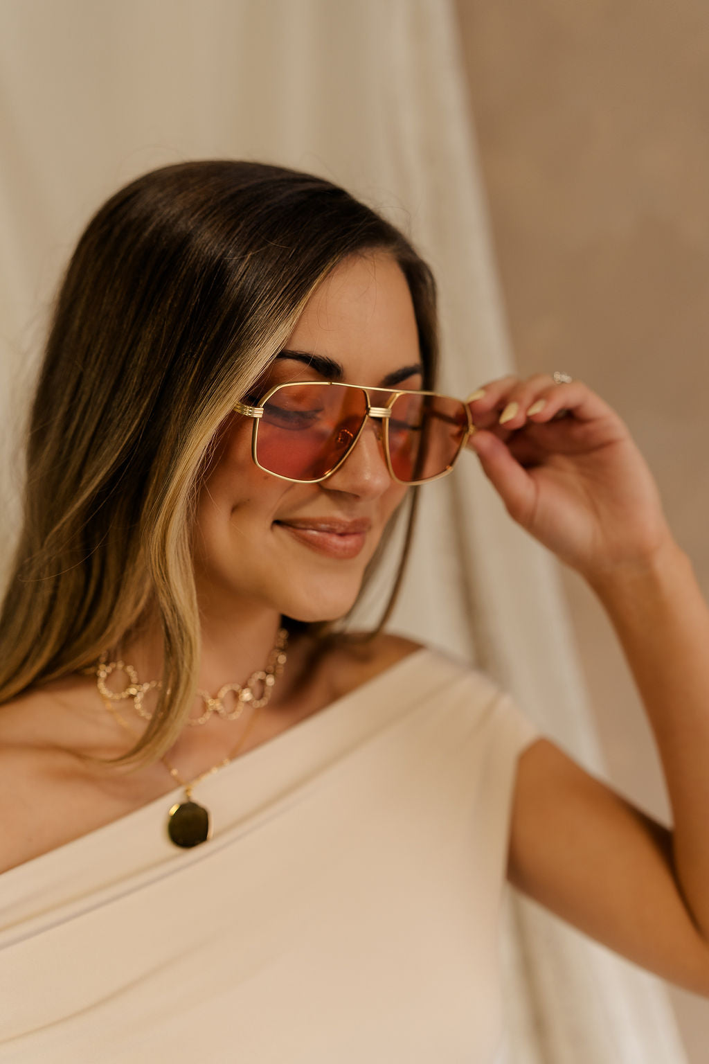 Upper body front view of female model. Model is wearing the The I-Sea: Bliss Sunglasses in Gold & Amber and a beige top.