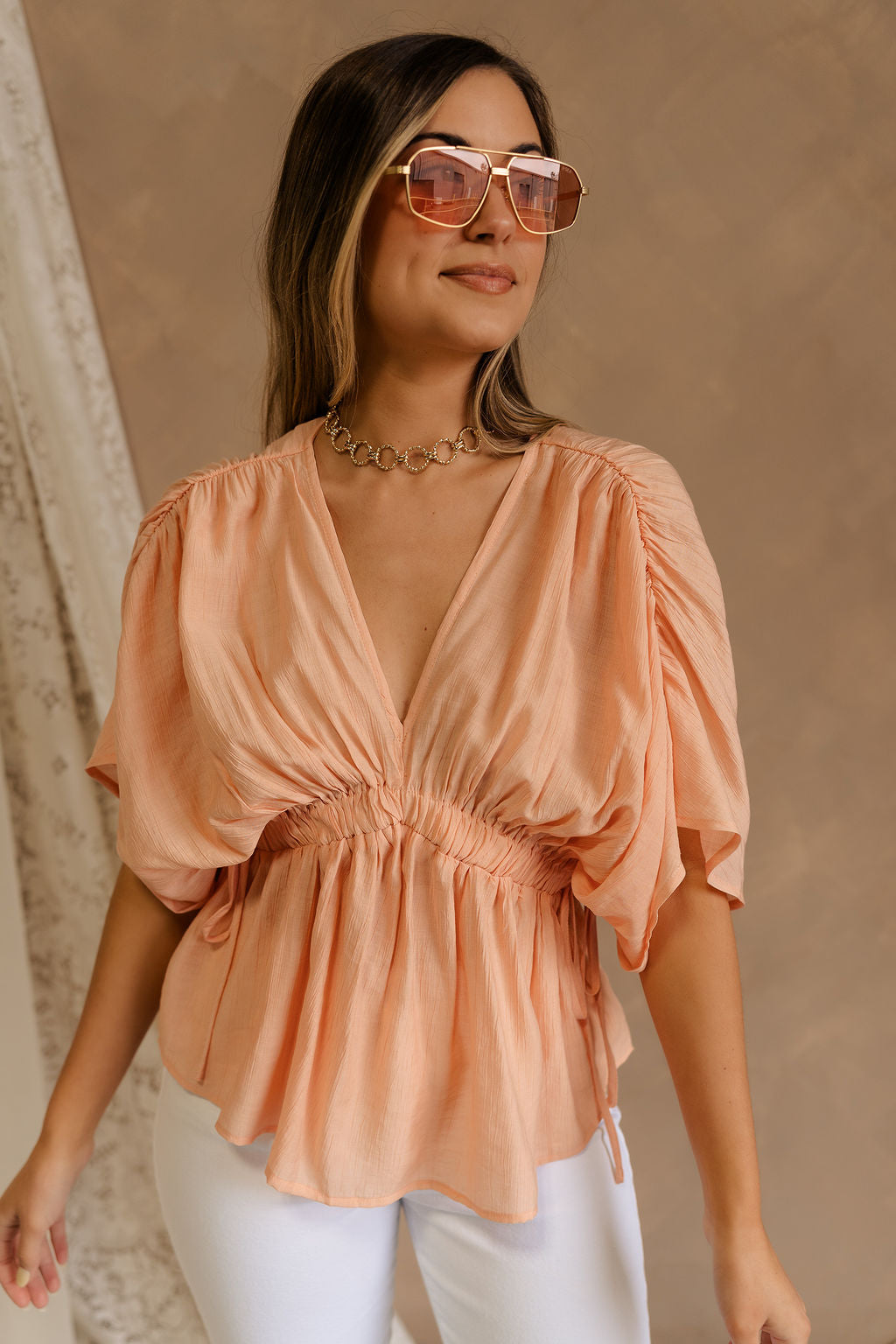 Front view of female model wearing the Juliet Peach Ruched Short Sleeve Top that features flowy peach fabric, ruched short sleeves, and an elastic waist.