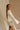 Side view of female model wearing the Kimberly Cream Pleated Long Sleeve Top which features Cream Sheer Plisse Fabric, Cropped Waist, Lettuce Hem Details, Round Neckline and Open Back with Tie Closures