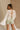Back view of female model wearing the Kimberly Cream Pleated Long Sleeve Top which features Cream Sheer Plisse Fabric, Cropped Waist, Lettuce Hem Details, Round Neckline and Open Back with Tie Closures