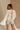 Back view of female model wearing the Kimberly Cream Pleated Long Sleeve Top which features Cream Sheer Plisse Fabric, Cropped Waist, Lettuce Hem Details, Round Neckline and Open Back with Tie Closures