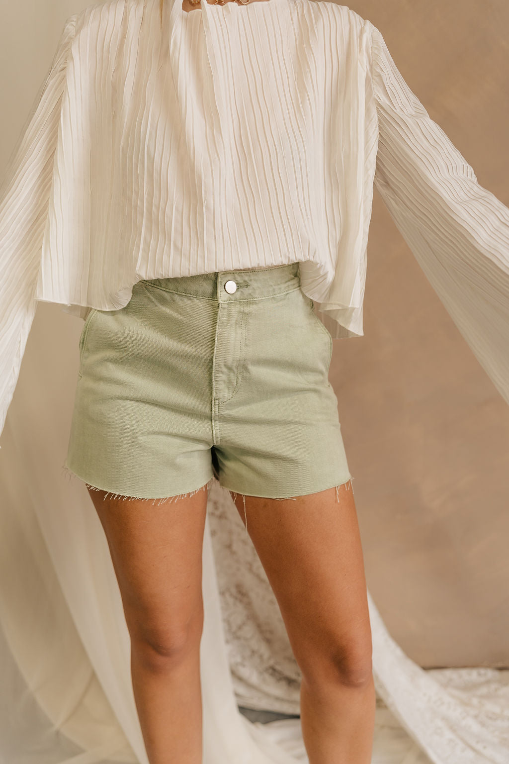 Front view of female model wearing the Paige Sage Denim Shorts which features Light Sage Denim Fabric, Two Front Pockets,Two Back Pockets, Fray Hem and Belt Loops.