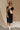 Full body front view of female model wearing the Remy Black Short Sleeve Midi Dress that features black knit fabric, short sleeves, midi length, and side slits. Worn with Rebecca Ivory Sling Bag.