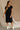 Full body front view of female model wearing the Remy Black Short Sleeve Midi Dress that features black knit fabric, short sleeves, midi length, and side slits. 