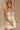 Front view of model sitting while wearing the Rosalind Cream & Black Sheer Tank that has cream sheer fabric, cream lining, black straps, and black tie and ruffle trim details. Worn with matching skirt.